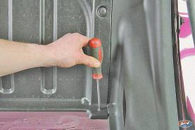 Выверните по два винта крепления панели, отделяющей салон от багажника на автомобиле Hyundai Solaris