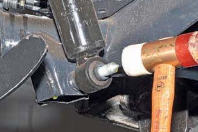 Молотком выбиваем болт нижнего крепления амортизатора к рычагу на автомобиле Hyundai Solaris