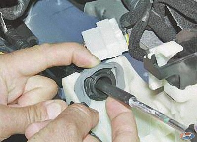 Отожмите фиксатор наконечника оболочки троса управления коробкой передач на автомобиле Hyundai Solaris