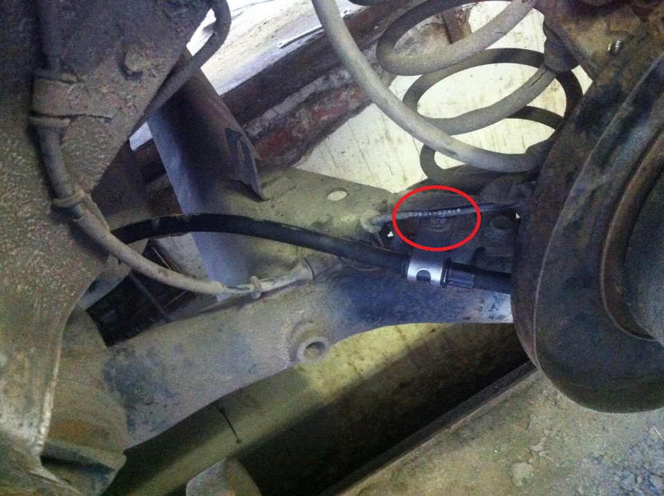 Отверните гайку, крепления оболочки троса привода стояночного тормоза к балке задней подвески на автомобиле Hyundai Solaris